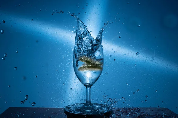 青い背景に水のガラスに落ちる石灰スライスの閉鎖 — ストック写真
