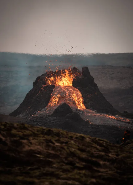 澄んだ空の下で溶岩と煙が流れる活火山の魅惑的な垂直ショット — ストック写真