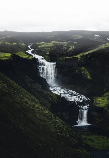緑の山々の上を滝が流れる川の魅惑的な垂直ショット — ストック写真