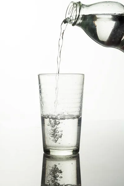 Вертикальный Снимок Процесса Разлива Воды Бутылки Стакан Белом Фоне — стоковое фото