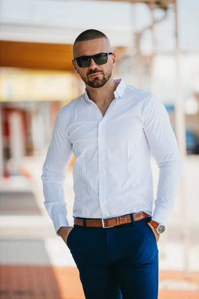 A cool handsome Caucasian man wearing an elegant white shirt and sunglasses posing outdoor