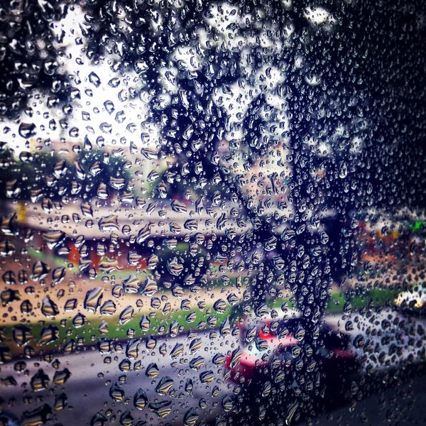 通りのぼやけた景色を望む窓に雨滴のクローズアップショット — ストック写真