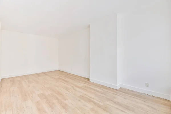 An interior shot of an empty room with white walls and a wooden floor