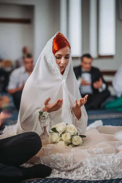 一个红头发的新娘头戴面纱 手持花束 在祭坛前祈祷的垂直镜头 — 图库照片
