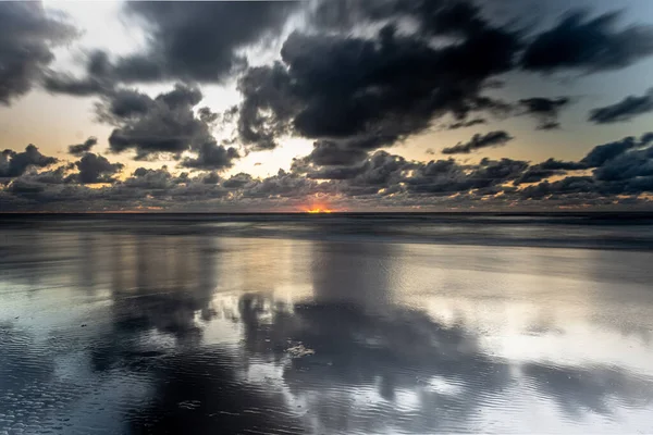 Ein Orangefarbener Sonnenuntergang Durch Dunkle Wolken Über Dem Ruhigen Meer — Stockfoto