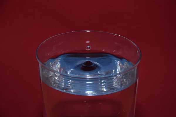 赤い背景に飛び散った液滴と それに青い反射を持つ水のガラスの閉鎖 — ストック写真