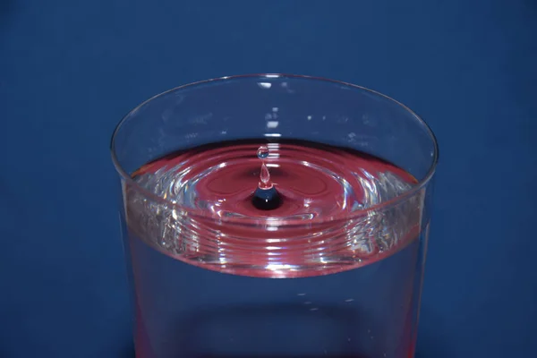 青い背景に飛び散る液滴と それに赤い反射を持つ水のガラスの閉鎖 — ストック写真