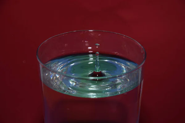 赤い背景に水滴が飛び散った水のガラスの塊 — ストック写真