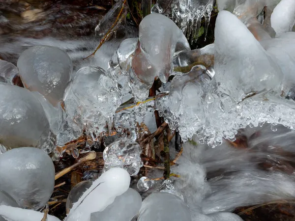 在一条小溪上挂在树枝上的冰雕 长期暴露在水面上 — 图库照片