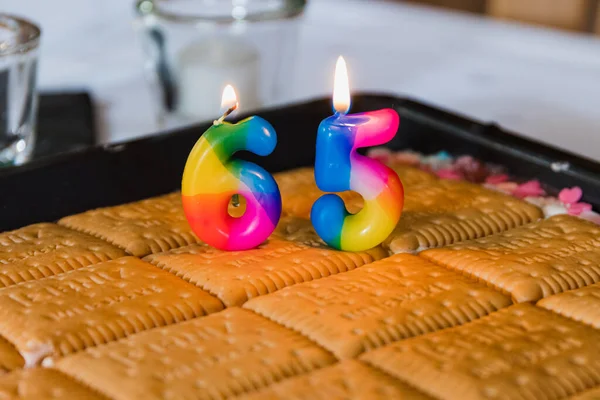 65歳の誕生日ケーキの上にキャンドルがあります 背景がぼやけているメガネもあります — ストック写真