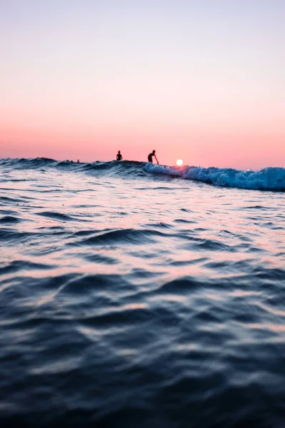 Gün Batımında Okyanusta Sörf Yapan Iki Kişinin Dikey Görüntüsü — Stok fotoğraf