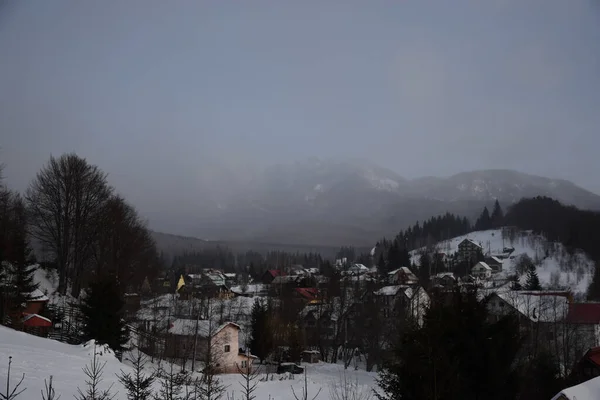 霧深い日に山や家に囲まれた雪に覆われた山々の風景 — ストック写真