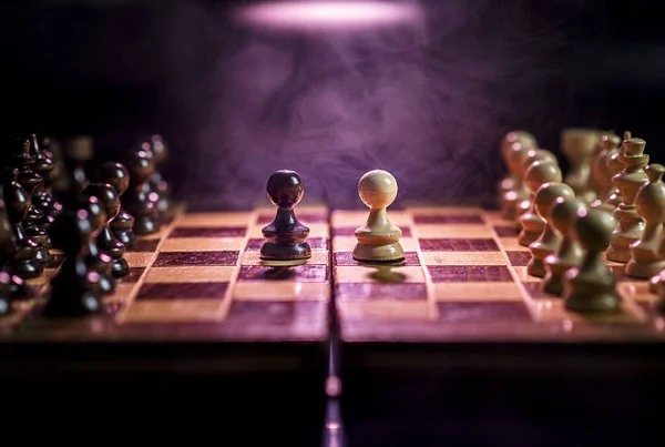 A closeup of chess pieces on the chessboard under the lights with a blurry background