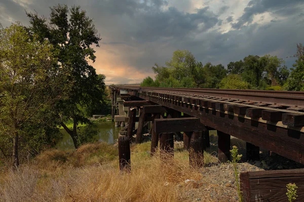 夕阳西下 一条旧的锈迹斑斑的铁路越过一条河 — 图库照片