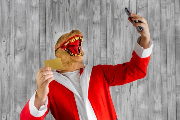 Dinozaur Przebrany Świętego Mikołaja Kartą Kredytową Komórką Ręku — Zdjęcie stockowe