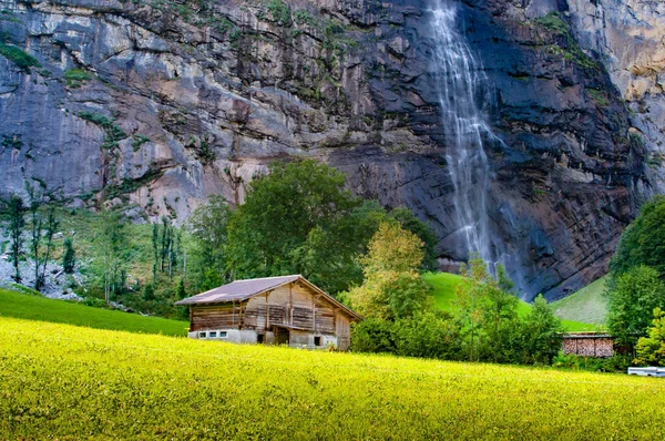 美しい風景緑の牧草地の土地 高い岩の山と背中の滝に木造の家 — ストック写真