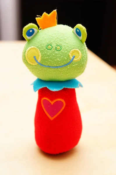 A vertical shot of a soft colorful frog toy isolated on the wooden table