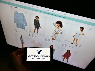STUTTGART, GERMANY - Jan 23, 2021: Person holding cellphone with logo of US retail company American Eagle Outfitters Inc. on display. Focus on phone screen. clipart
