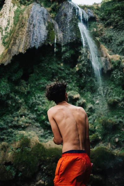 一个赤身裸体的男人站在瀑布前的垂直镜头 — 图库照片
