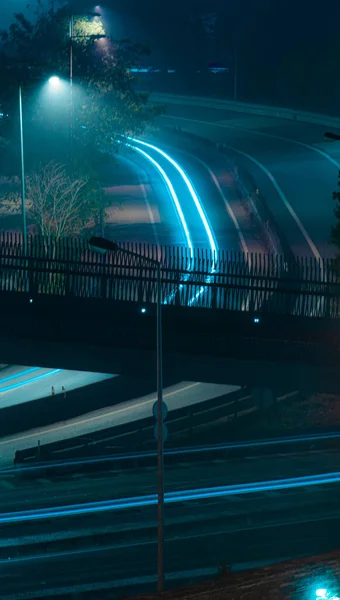 在道路上方有霓虹灯的一座桥的垂直截图 夜间暴露时间长 — 图库照片