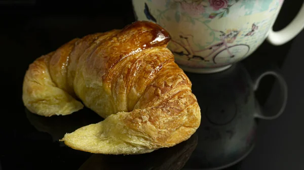 Närbild Croissant Och Dekorerad Kopp Svart Reflekterande Bas — Stockfoto