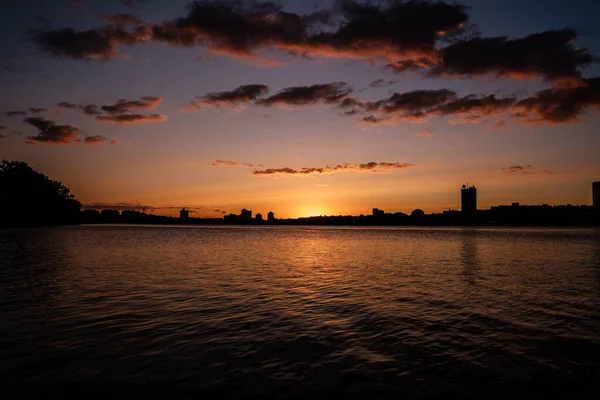 曇った空に向かって前景に湖の水で夕日を眺める魅惑的な街並み — ストック写真