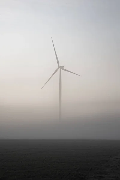 Vertikální Záběr Větrné Turbíny Poli Mlhavého Dne Při Východu Slunce — Stock fotografie