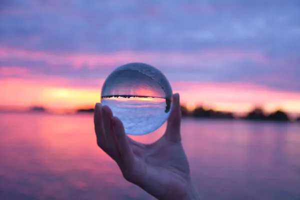 A hand holding a glass ball with reflection of a sunset at Rhine