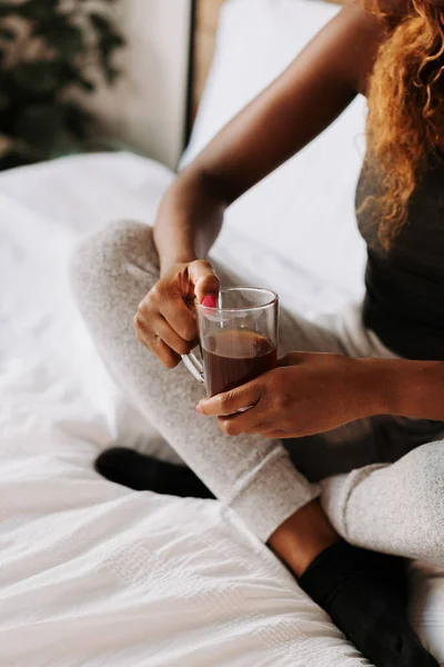 黒の女性がベッドでコーヒーを飲む垂直ショット — ストック写真