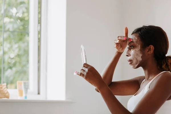 Young Beautiful Black Female Holding Mirror Applying Mask Her Face — ストック写真