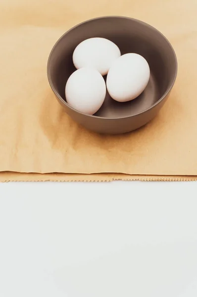 食物紙の上の濃い灰色のボウルの中の有機的な白い卵とテキストのためのコピースペースを持つ白い表面 — ストック写真