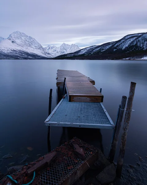 背後に氷の山のある湖の上に古い木製の桟橋 — ストック写真