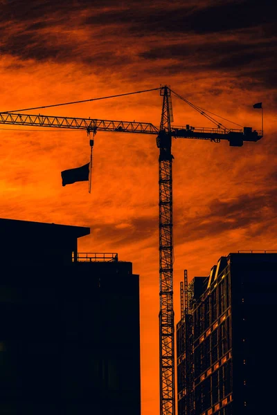 A vertical shot of an American flag hanging on a crane in a bright orange sunset sky