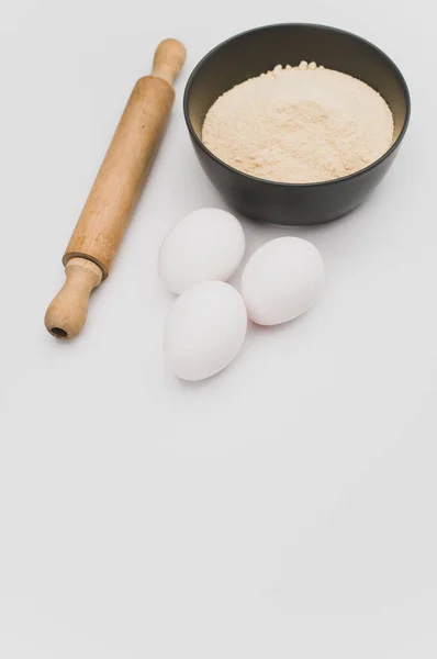 木製のローリングピン白い卵とコピースペースと白い背景に全粒小麦粉と濃い灰色のボウル — ストック写真