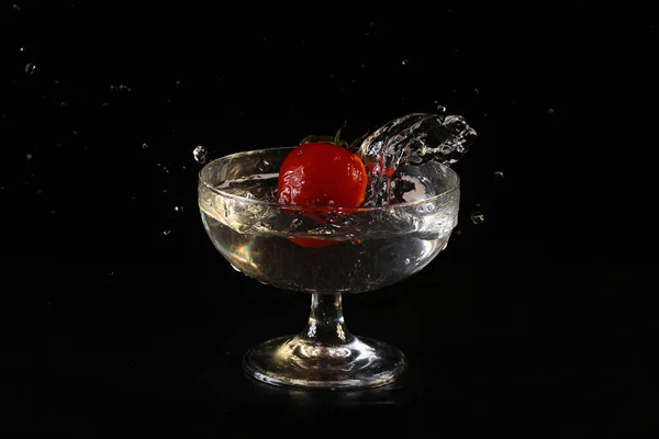 桜のトマトがガラスの水の中に落ちる — ストック写真