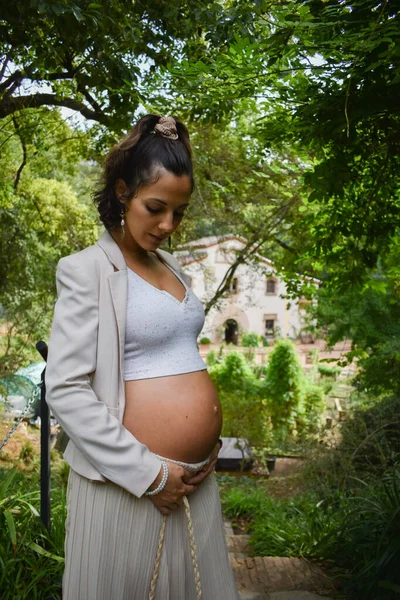 一个时髦的白人孕妇站在花园里抱着肚子 — 图库照片