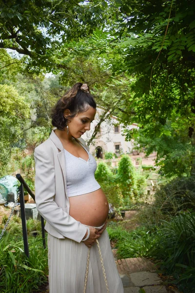一个白人孕妇抱着肚子站在花园里 — 图库照片