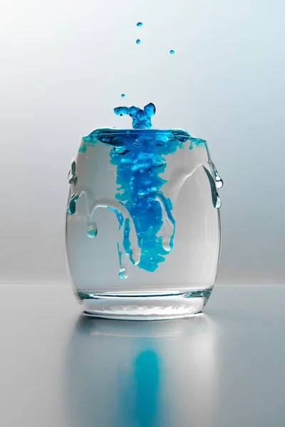 一杯带有水花和蓝色油漆的水的垂直截图 — 图库照片