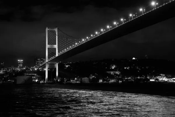 一座被现代建筑环绕的海上照明悬索桥的灰度照片 — 图库照片