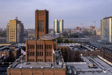 Front exterior facade of Inktpot bricked building with UFO resting on it at sunrise with central train station and shiny architecture of Utrecht clipart