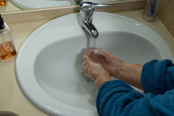 バスルームの石鹸で手を洗う女性の手は青いバスローブに沈む — ストック写真