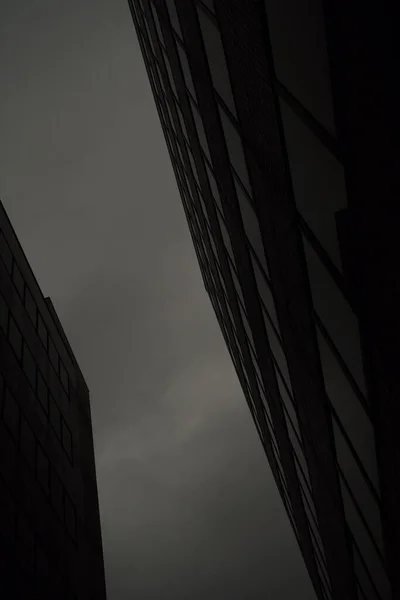 Eine Vertikale Graustufenaufnahme Von Wolkenkratzern Unter Einem Bewölkten Dunklen Himmel — Stockfoto