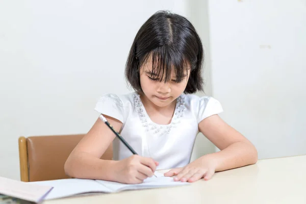 Маленькая Азиатская Девочка Сидит Столом Пишет Блокноте Белом Фоне — стоковое фото