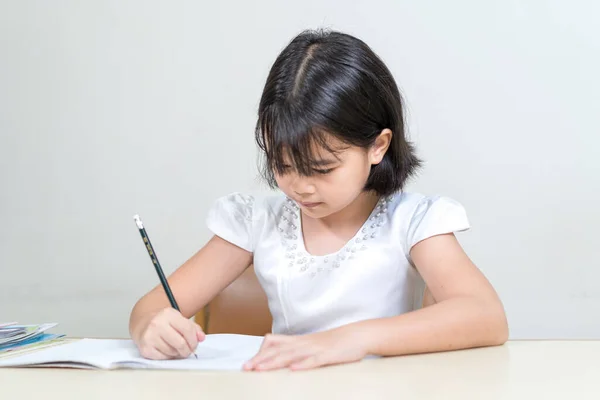 Маленькая Азиатская Девочка Сидит Столом Пишет Блокноте Белом Фоне — стоковое фото