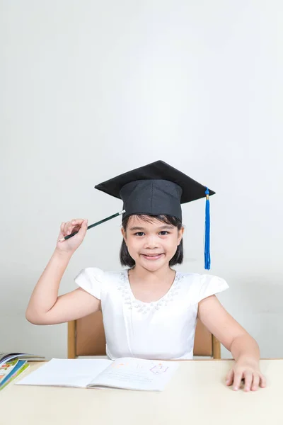 Cheerful Asian Little Girl Mortarboard Sitting Her Desk White Background — Stock Photo, Image