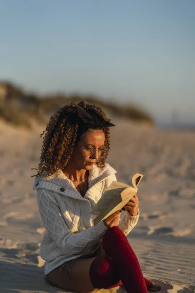 Vertical Shot Spanish Curly Female Reading Book While Sitting Sand — Fotografia de Stock