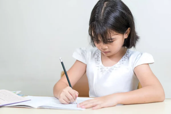 Азіатська Дівчинка Сидить Столом Пише Своїй Книзі Білому Тлі — стокове фото