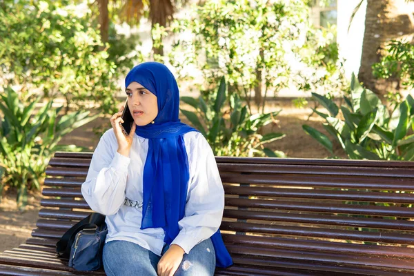 Молодая Мусульманка Хиджабе Сидит Скамейке Парке Разговаривает Телефону Копирует Спа — стоковое фото