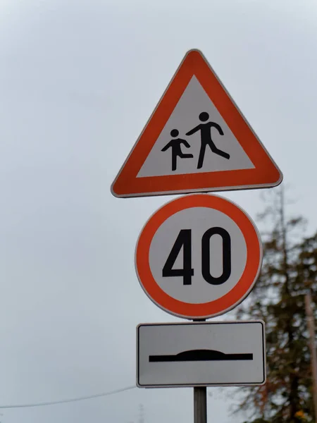 A warning pedestrian crossing sign, round speed limit 40 sign, and hump sign on a pole