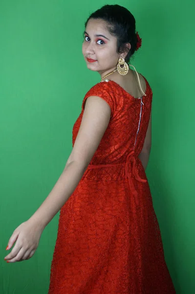 一个漂亮的女人 穿着一件红色的衣服 戴着珠宝 在绿色的墙壁上化妆 — 图库照片